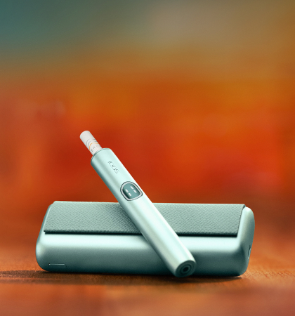 An IQOS device held by one person and a smartphone held by another person.